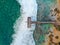 Aerial view of dock over tropical blue water and sand beach, with waves.