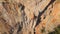 aerial view from drone of strong muscular young man climbs on big rocky wall by challenging rock climbing route.