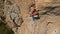 aerial view from drone of strong muscular young man climbs on big rocky wall by challenging rock climbing route.