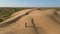 Aerial view from a drone. Woman in a long leopard dress walks along a high dune in the desert with grass in summer in