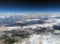 Aerial view of the earth from high altitude with dark blue sky and different types of white clouds with snow on a hilly landscape