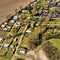 Aerial view of the edge of a campsite with a few cottages, caravans and tents on grassland