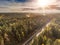 Aerial view on a empty road going through a forest. Sun flare, Nobody, Blue cloudy sky. Fog rises to the sky