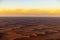 Aerial view of an expansive desert landscape, with sandy dunes and billowing clouds