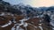 Aerial view of a fast downward movement over a road near an old rural house in a valley with snow and high mountains in front