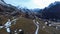 Aerial view of a fast upward movement over a road near an old rural house in a valley with snow and high mountains in front