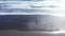 Aerial view of a female traveler relaxing on Atlantic ocean coast. Sea waves washing black sandy beach, reflection of clouds