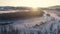 Aerial view: flight along a frozen river in the mountains. Beautiful sunrise. A village on the shore, snow-covered roofs