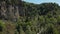 Aerial view of the flight of the camera over a deep rocky gorge with high cliffs and a dense forest and a river flowing