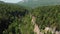 Aerial view of the flight of the camera over a deep rocky gorge with high cliffs and a dense forest and a river flowing