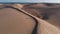 Aerial view - flight of a drone in front of a girl in summer white clothes running through the hot desert on a sunny day