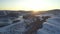 Aerial view: Flight over the village by the river in winter. Beautiful sunrise in the mountains. Snow-covered roofs of