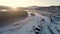 Aerial view: flight over the village by the river in winter. Beautiful sunrise in the mountains. Snow-covered roofs of