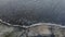 Aerial view, flying over coastline during a storm. Camera moves downwards above rocky shore and sea waves with foam