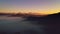 Aerial view of fog coverage the mountains forest at sunrise. Distant mountain range and thin layer of clouds on the valleys