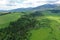 Aerial view of forested depression between two grassland fields during summer cloudy day, High Tatras mountains in background.