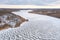 Aerial view of a frozen and snowy river, a winter landscape, snow in the form of a wave was blown away by the wind along the