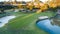 Aerial view of golf course green with flag, bunkers and dam water hazards surrounded by trees in background