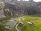 Aerial view of a grassy valley and alpine range features several cabins in the valley