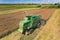 Aerial view of a green agricultural combine with a revolving reel harvesting crop in a large grain field. Tractors with