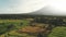 Aerial view, green fields and active volcano. Palms and trees summer backlit, plots land wilderness.