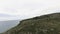 Aerial view of green hills and stones on cloudy sky and sea background. Shot. Flying above beautiful mountain top.