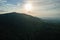 Aerial view of green pine forest with dark spruce trees covering mountain hills at sunset. Nothern woodland scenery from