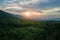 Aerial view of green pine forest with dark spruce trees covering mountain hills at sunset. Nothern woodland scenery from