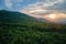 Aerial view of green pine forest with dark spruce trees covering mountain hills at sunset. Nothern woodland scenery from