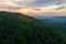 Aerial view of green pine forest with dark spruce trees covering mountain hills at sunset. Nothern woodland scenery from