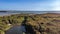 An aerial view of the Hengistbury Head hill with pond, trails, colorful vegetations and the blue sea and harbor in the background