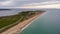 An aerial view of the Hengistbury Head with majestic sandy beach, crystal green water, grassy hill, huge cliff with the harbor and