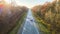 Aerial view of intercity road with fast driving car between autumn forest trees at sunset. Top view from drone of