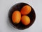 Aerial view of kumquats, cumquats, in black ceramic bowl against white background.