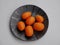 Aerial view of kumquats, cumquats, on black ceramic plate against white background.