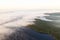 Aerial view lake with fog above water surface and sunrise over forest. Top view amazing seashore with fog over the water and green