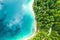 Aerial view of a lake with turquoise water and clouds reflection and pine trees on the shore