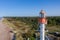 Aerial view of lighthouse with red top and white base. Blue sky and sea. Pape lighthouse