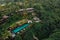 Aerial view of luxury hotel with straw roof villas and pools in tropical jungle and palm trees. Luxurious villa, pavilion in