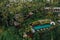 Aerial view of luxury hotel with straw roof villas and pools in tropical jungle and palm trees. Luxurious villa, pavilion in