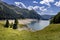 Aerial view of the Luzzone lake during a dry period. In the foreground is a group of fir trees, and in the background is