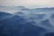 Aerial view of misty mountains and clouds above the mountain peaks, blue tinted