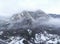 Aerial view of mountain with boundary tower, forest underneath fog, slopes with snow covered in Switzerland, cloudy