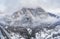 Aerial view of mountain with boundary tower, forest underneath fog, slopes with snow covered in Switzerland, cloudy