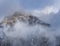 Aerial view of mountain with boundary tower, forest underneath fog, slopes with snow covered in Switzerland, cloudy