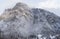 Aerial view of mountain with boundary tower, forest underneath fog, slopes with snow covered in Switzerland, cloudy