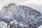 Aerial view of mountain with boundary tower, forest underneath fog, slopes with snow covered in Switzerland, cloudy