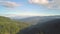 Aerial view of mountains covered with forest trees with blue sky above.