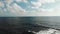 Aerial view of ocean sea horizon with blue sky and clouds. Strong waves hitting rocky beach creating foam and splashing