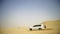 Aerial view on Off-road adventure with SUV in Arabian Desert at sunset with Dubai skyline or cityscape. Desert touring